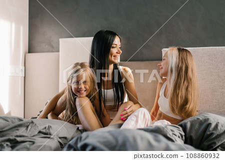 Happy family mom and daughters in pajamas in the morning in bed having fun and chatting 108860932