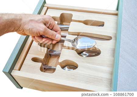 Man puts spoon in craved wooden holder in cabinet drawer Man puts spoon in craved wooden holder in cabinet drawer 108861700