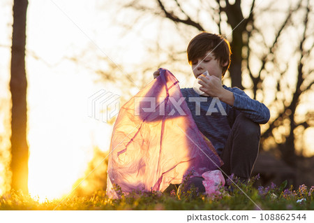Cute teenage boy collects garbage in big bag in nature, in meadow on autumn evening at sunset. Environmental problems. 108862544