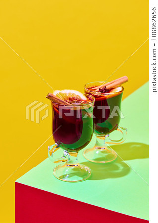 Glasses with delicious red mulled wine with oranges and cinnamon against colorful background. Traditional hot drink in winter season. Poster Glasses with delicious red mulled wine with oranges and cinnamon against colorful background. Traditional hot drink in winter season. Poster 108862656