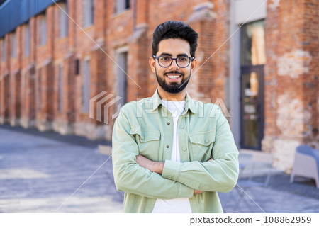 Portrait of young man in casual clothes joyful businessman smiling and looking at camera with arms crossed, Indian man outside office building. Portrait of young man in casual clothes joyful businessman smiling and looking at camera with arms crossed, Indian man outside office building. 108862959