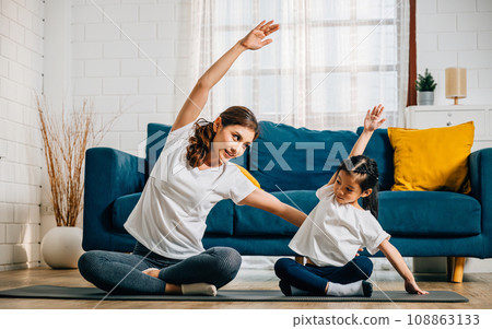 In a heartwarming family yoga session a mother and her daughter work on stretch and balance finding harmony and happiness with smiles reflecting their togetherness. 108863133