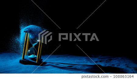 Hourglass is sand of time age, Life pour blue sand into hourglass to add more limited time. Deadline extended time management hope concept hour glass. Black background shadow life clock passing by 108863164