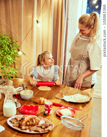 Happy family time. Young woman, mother cooking with little girl, daughter in modern kitchen at home. Cooking croissants and cookies 108863366