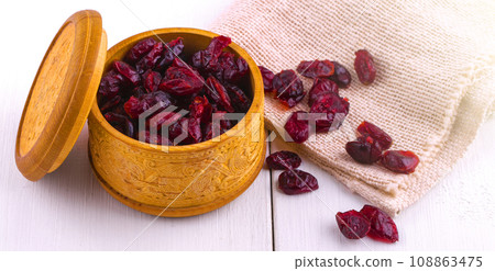 Dried cranberries in a wooden cup with a lid and burlap on a white wooden table Dried cranberries in a wooden cup with a lid and burlap on a white wooden table 108863475
