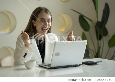 Happy excited woman at home workstation triumphing with raised hands Happy excited woman at home workstation triumphing with raised hands 108864750