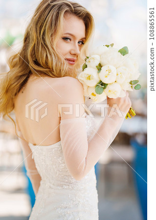 Beautiful blonde bride in a tight-fitting dress with a bouquet.  108865561