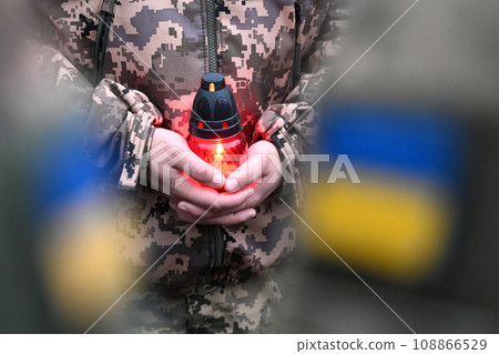 A Ukrainian seviceman holds a candle. Ukrainian flag on military uniform. Candle in hands of Soldier 108866529