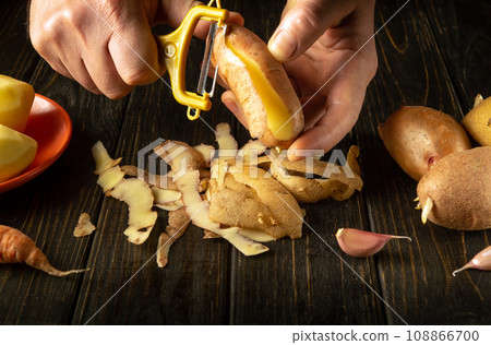 The chef peels potato for mashed potatoes. Vegetable diet idea. Potatoes menu concept on black table 108866700
