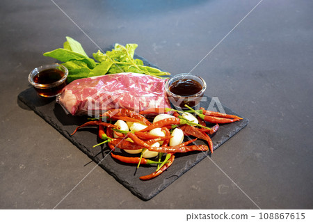 Raw Beef and herb ingredients, basil leaf, garlic, chilli, sauces are prepared on a black stone, slate plate for next cooking process in the Thai food menu, Stir-fried beef basil. Raw Beef and herb ingredients, basil leaf, garlic, chilli, sauces are prepared on a black stone, slate plate for next cooking process in the Thai food menu, Stir-fried beef basil. 108867615