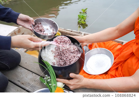 The monk was Holding monk's alms-bowl, between Thai Local people make merit by offering food rice to the monk who in a vintage wooden boat in the morning. The monk was Holding monk's alms-bowl, between Thai Local people make merit by offering food rice to the monk who in a vintage wooden boat in the morning. 108868824