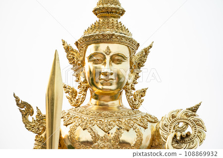 A golden graven image standing with a sword and rowel in his hand. Jada's multiple layers are placed on his head. He was standing on golden bases against a white backdrop A golden graven image standing with a sword and rowel in his hand. Jada's multiple layers are placed on his head. He was standing on golden bases against a white backdrop 108869932