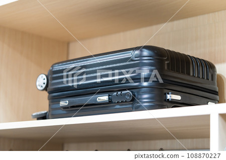 A black suitcase placed at the top of a white brown wood shelf. A black suitcase placed at the top of a white brown wood shelf. 108870227
