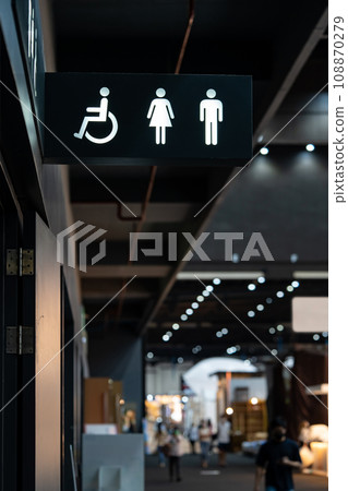 A sign of restroom lighten in white standout from a black plate. The restroom is inside a building, decorated in black and white tone. A sign of restroom lighten in white standout from a black plate. The restroom is inside a building, decorated in black and white tone. 108870279