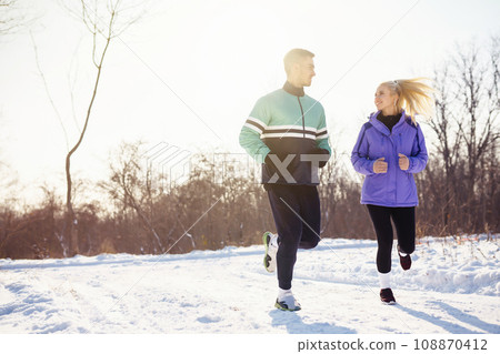 Young couple in sportswear doing morning exercise at snowy forest. Healthy lifestyle concept. 108870412
