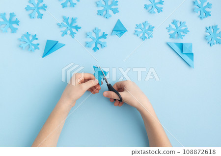 Hands making paper snowflakes on blue child hands Hands making paper snowflakes on blue child hands 108872618