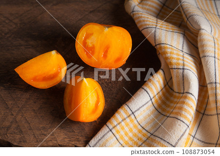 Cut and whole of yellow tomato and yellow towel on wooden background.. 108873054