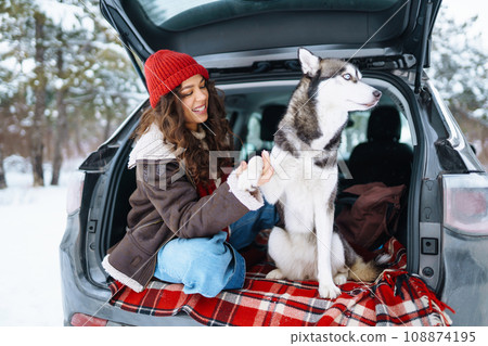 Young woman and cute husky dog enjoying outdoors into the car. Travel concept. Winter season. Young woman and cute husky dog enjoying outdoors into the car. Travel concept. Winter season. 108874195