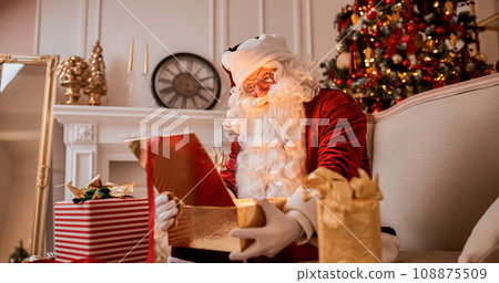 Surprised Santa Claus with glowing gift near christmas tree. New year and Merry Christmas concept Surprised Santa Claus with glowing gift near christmas tree. New year and Merry Christmas concept 108875509