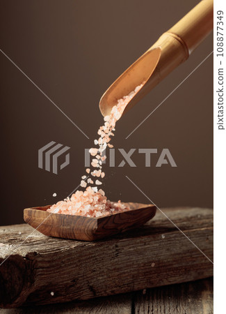 Pink salt is poured with a wooden spoon in the wooden dish. 108877349