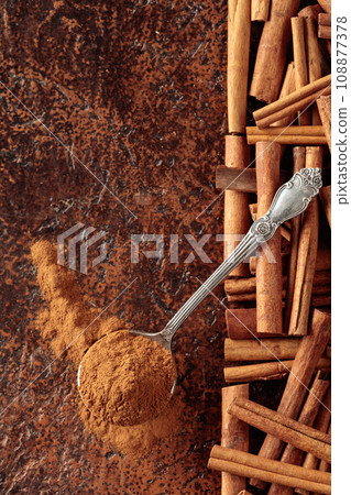 Cinnamon powder in a spoon and cinnamon sticks on a brown background. 108877378