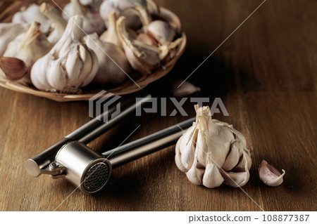 Garlic bulbs and garlic press on a wooden table. 108877387