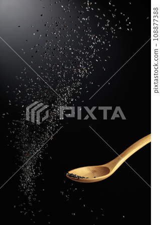 Grains of black sesame is poured with a wooden spoon. 108877388