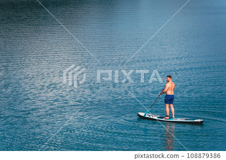 man balancing on supboard paddling 108879386