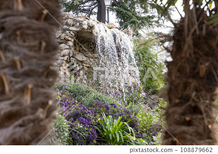Waterfall. Waterfall in a park in Madrid. Artificial Mountain of Buen Retiro, called Mountain of the Cats. Dark stone background surrounded by green vegetation and plants and leaves. Autumn colors. Waterfall. Waterfall in a park in Madrid. Artificial Mountain of Buen Retiro, called Mountain of the Cats. Dark stone background surrounded by green vegetation and plants and leaves. Autumn colors. 108879662