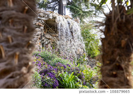 Waterfall. Waterfall in a park in Madrid. Artificial Mountain of Buen Retiro, called Mountain of the Cats. Dark stone background surrounded by green vegetation and plants and leaves. Autumn colors. 108879665