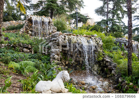 Waterfall. Waterfall in a park in Madrid. Artificial Mountain of Buen Retiro, called Mountain of the Cats. Dark stone background surrounded by green vegetation and plants and leaves. Autumn colors. 108879666