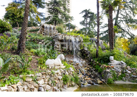 Waterfall. Waterfall in a park in Madrid. Artificial Mountain of Buen Retiro, called Mountain of the Cats. Dark stone background surrounded by green vegetation and plants and leaves. Autumn colors. 108879670