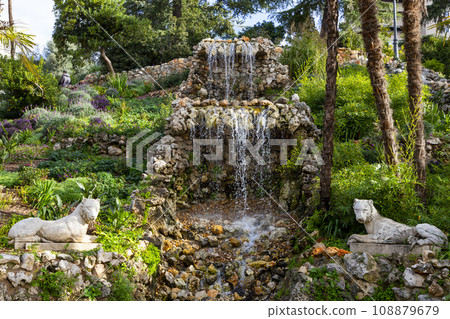 Waterfall. Waterfall in a park in Madrid. Artificial Mountain of Buen Retiro, called Mountain of the Cats. Dark stone background surrounded by green vegetation and plants and leaves. Autumn colors. 108879679