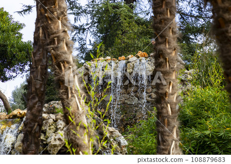 Waterfall. Waterfall in a park in Madrid. Artificial Mountain of Buen Retiro, called Mountain of the Cats. Dark stone background surrounded by green vegetation and plants and leaves. Autumn colors. 108879683