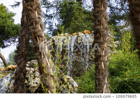 Waterfall. Waterfall in a park in Madrid. Artificial Mountain of Buen Retiro, called Mountain of the Cats. Dark stone background surrounded by green vegetation and plants and leaves. Autumn colors. 108879685
