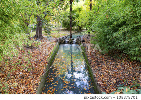 Waterfall. Waterfall in a park in Madrid. Artificial Mountain of Buen Retiro, called Mountain of the Cats. Dark stone background surrounded by green vegetation and plants and leaves. Autumn colors. 108879701
