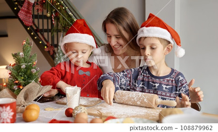 Happy mother helping their sons cooking Christmas cookies and biscuits for celebrations. Winter holidays, celebrations and party. Happy mother helping their sons cooking Christmas cookies and biscuits for celebrations. Winter holidays, celebrations and party. 108879962