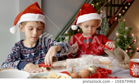 Portrait of two little boys in SAnta hats enjoying rolling dough and cutting out Christmas cookies and ginger bread for New Year celebrations Portrait of two little boys in SAnta hats enjoying rolling dough and cutting out Christmas cookies and ginger bread for New Year celebrations 108879968