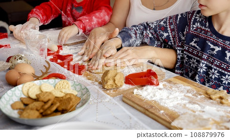 Closeup of mother showing her kids how to make cookies and ginger bread for Christmas on kitchen. Winter holidays, celebrations and party. Closeup of mother showing her kids how to make cookies and ginger bread for Christmas on kitchen. Winter holidays, celebrations and party. 108879976