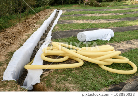 Yellow corrugated pipe with perforation in a trench with crushed stone and geotextile. Drainage works for the removal of ground water. Yellow corrugated pipe with perforation in a trench with crushed stone and geotextile. Drainage works for the removal of ground water. 108880028