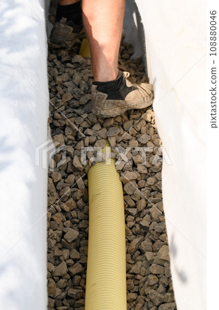 A worker stands in a drainage trench with white geotextile. Feet of the craftsman on the granite rubble closeup. A worker stands in a drainage trench with white geotextile. Feet of the craftsman on the granite rubble closeup. 108880046