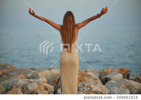 Cute stylish girl posing on the beach. The girl is dressed in a stylish off-the-shoulder dress. She's wearing brown sunglasses. The ocean is behind her. Cute stylish girl posing on the beach. The girl is dressed in a stylish off-the-shoulder dress. She's wearing brown sunglasses. The ocean is behind her. 108881818