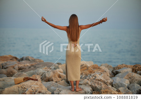 Cute stylish girl posing on the beach. The girl is dressed in a stylish off-the-shoulder dress. She's wearing brown sunglasses. The ocean is behind her. Cute stylish girl posing on the beach. The girl is dressed in a stylish off-the-shoulder dress. She's wearing brown sunglasses. The ocean is behind her. 108881819