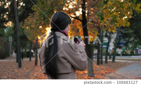 Woman sipping coffee as waiting for business meeting in town park in autumn Woman sipping coffee as waiting for business meeting in town park in autumn 108883127