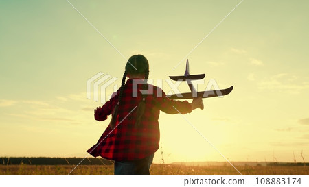 Little girl silhouette plays with plane running in meadow at back sunset light Little girl silhouette plays with plane running in meadow at back sunset light 108883174