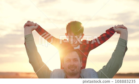 Father carries son on shoulders at back sunset on family vacation in countryside Father carries son on shoulders at back sunset on family vacation in countryside 108883235