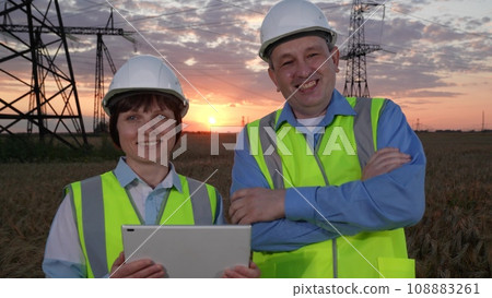 Engineers with tablet smile to camera against electric power generation plant 108883261