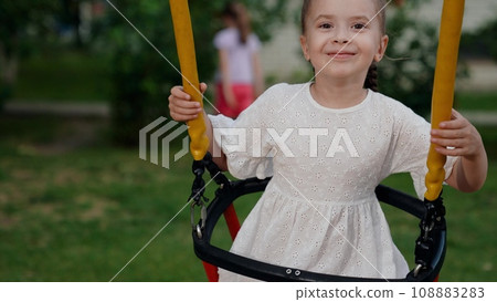 Cute little girl with gap toothed smile plays swings on city playground closeup 108883283