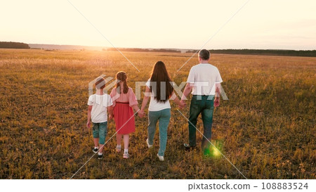 Positive parents with little children walk joining hands across sunset field 108883524