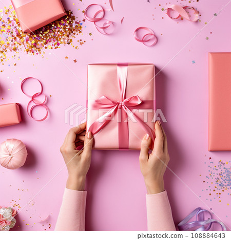Female hands hold a pink gift box with a satin bow on a pink background 108884643